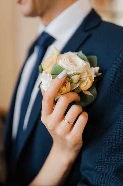 The bride gently adjusts the boutonniere of the groom in a blue suit closeup