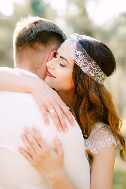 The bride gently hugs the groom in the park and smiles closeup