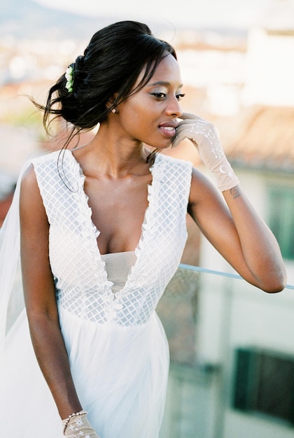 Bride in gloves touches her cheek with her fingers on the roof of the house