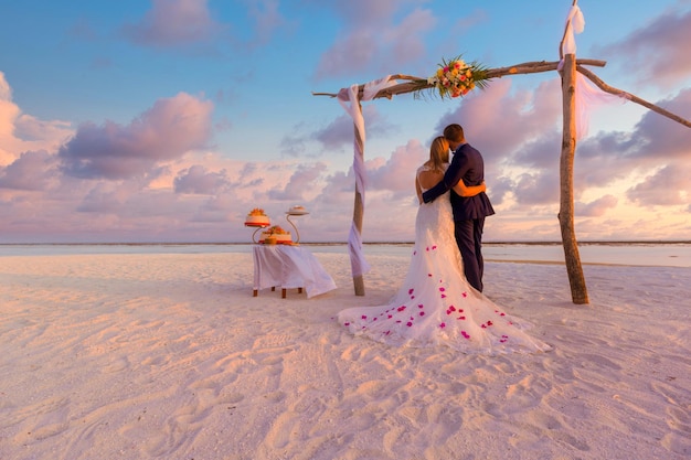 The bride and groom under archway on beach. Romantic destination wedding anniversary background