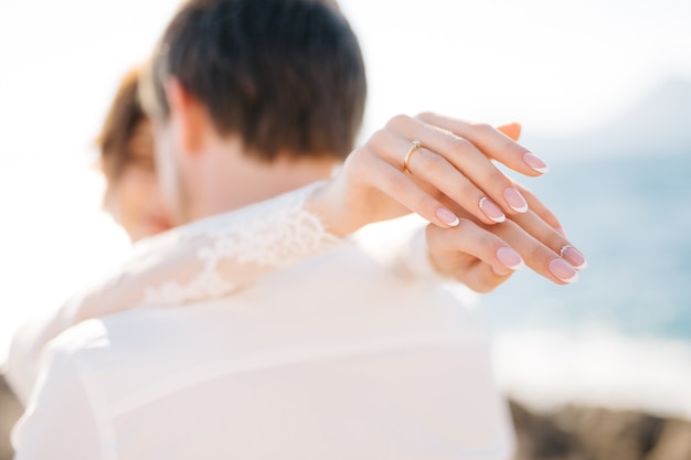 花嫁と花婿はマムラ島の岩の多いビーチで抱きしめています、花嫁は花婿の肩に手を置きます