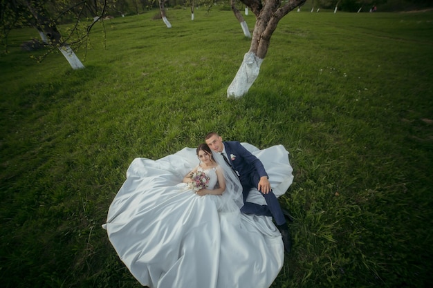 A bride and groom are lying on the grass with the bride holding a bouquet