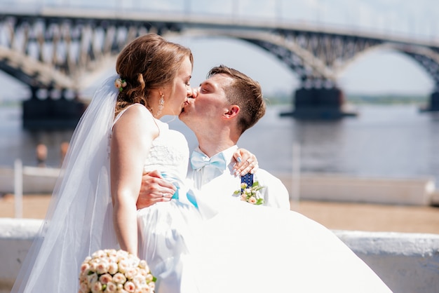 The bride and groom are photographed on the background of the bridge