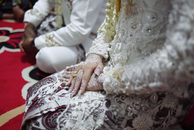 A bride and groom are sitting on the floor, wearing a white dress with gold embroidery.