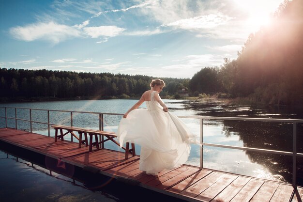 新郎新婦が湖の橋の上に立っています。夫婦。美しい結婚式のカップルのキスと湖の近くの橋でポーズ