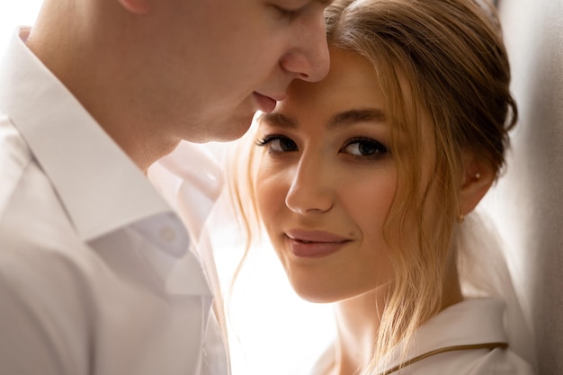 A bride and groom are standing in front of a window, the man is wearing a white shirt and the man is wearing a white shirt.