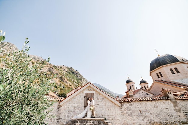 Bride and groom are standing on the steps at the door of the stone fence of the church of st