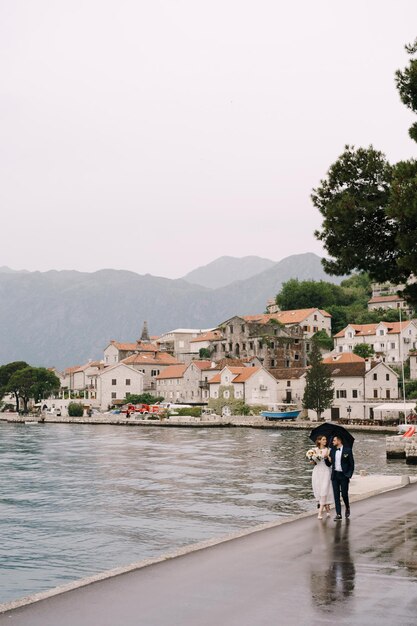 Жених и невеста гуляют по набережной старого города под зонтиком