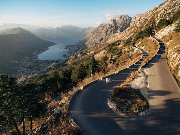 Gli sposi stanno camminando lungo una strada asfaltata di alta montagna sopra la baia