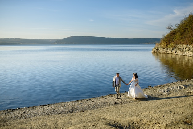 The bride and groom are walking near the lake on the shore