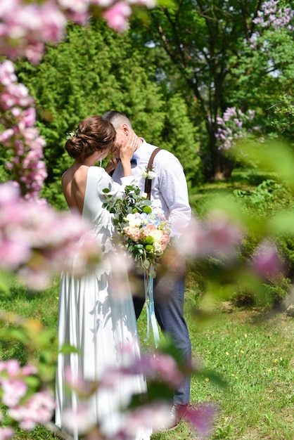 花束の新郎新婦は緑豊かな公園でキスします。