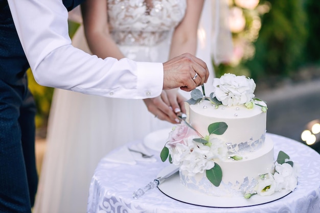 The bride and groom cut out a piece of a large and delicious cake with a knife