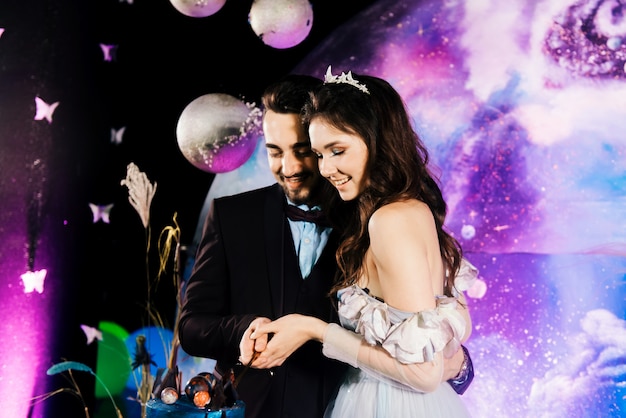 The bride and groom cut a space wedding cake decorated with chocolate and planets. The concept of festive desserts for the holiday