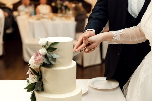 The bride and groom cut their rustic wedding cake at the wedding banquet. close-up hands cutting a beautiful cake