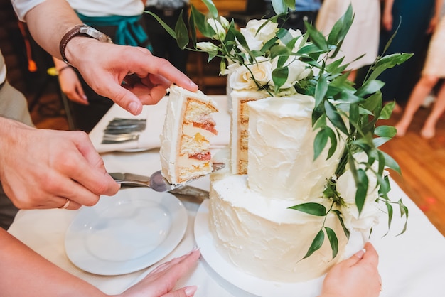 Bride and groom cutting beautiful wedding cake decorated with leaves