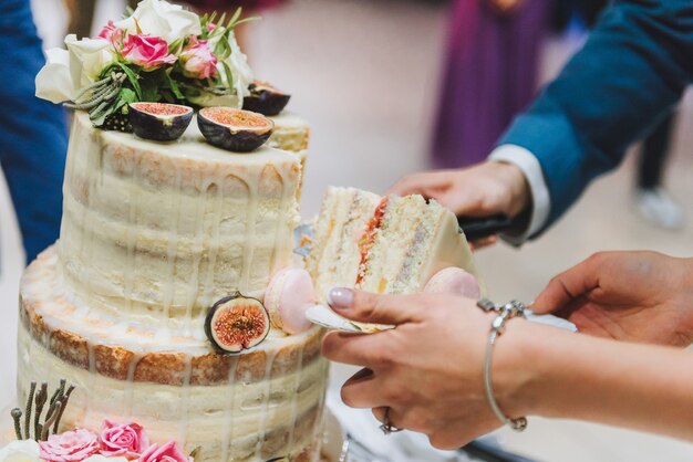 イチジクフルーツ、マカロンと花で飾られた新郎新婦のウェディングケーキのカット