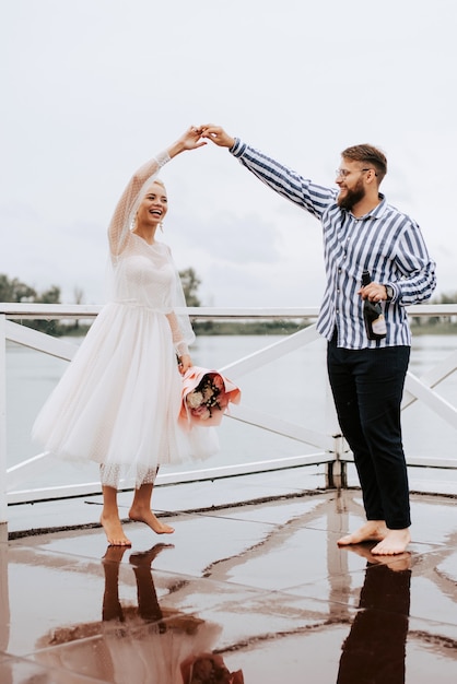 The bride and groom dance barefoot and have fun on the wharf by the river.