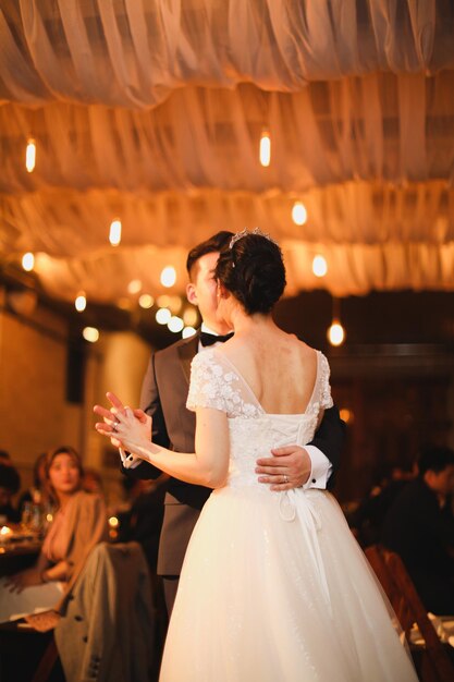A bride and groom dance in front of a chandelier with lights