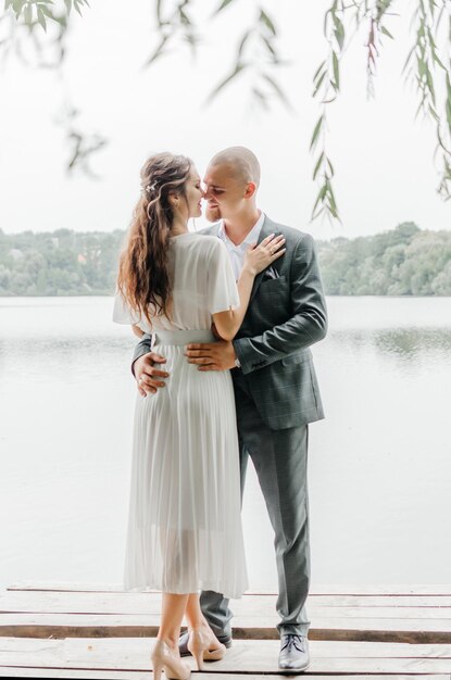 the bride and groom embrace and kiss on the shore of the lake