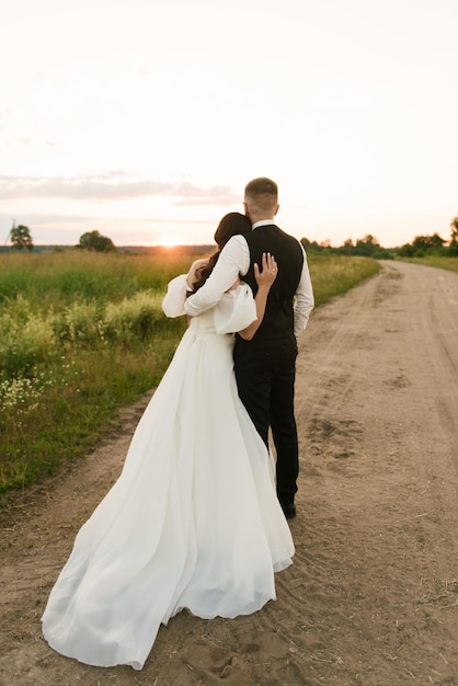 The bride and groom embrace stand with their backs to the sunset