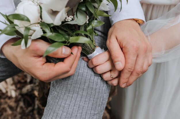 Foto la sposa e lo sposo si tengono dolcemente per mano, tengono un bouquet in mano.