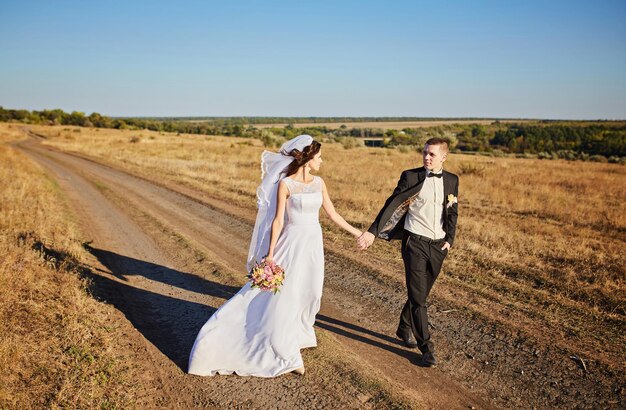 Жених и невеста идут по полю рука об руку