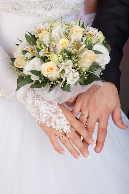 Bride and groom hands with wedding rings and bouquet of roses