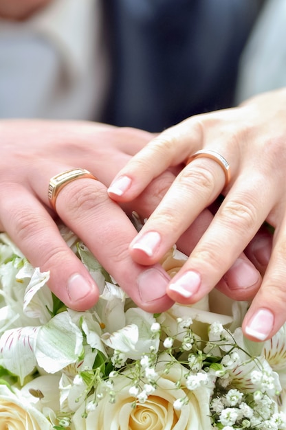 The bride and groom hold hands with wedding rings on the bouquet