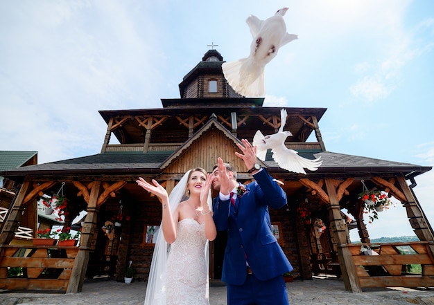 Bride and groom hold pigeons standing before a wooden church