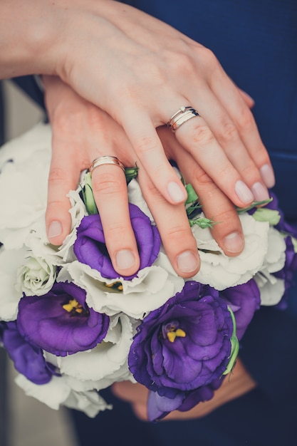 La sposa e lo sposo tengono le loro mani con gli anelli sopra un mazzo di nozze con i fiori blu e bianchi