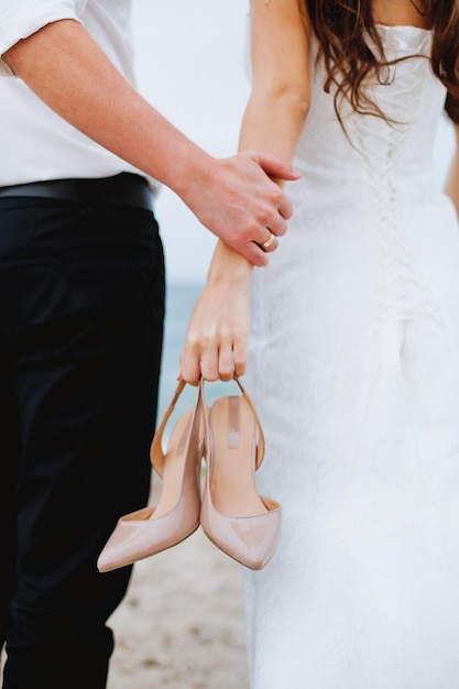 A bride and groom hold their shoes on the beach.