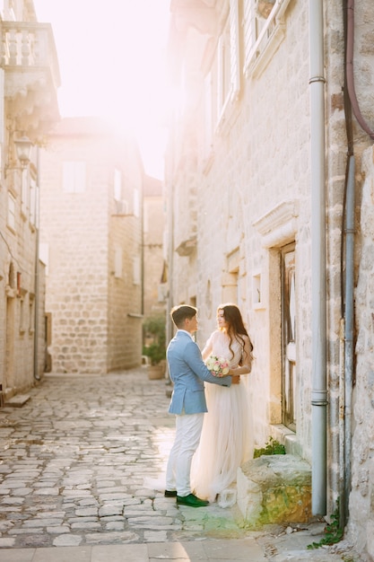 The bride and groom hug on a beautiful old street of perast near a white stone wall