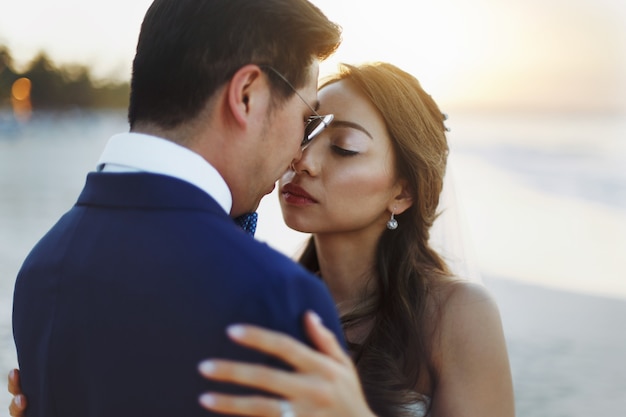 Bride and groom hug each other tender standing in the rays of golden sun on the beach