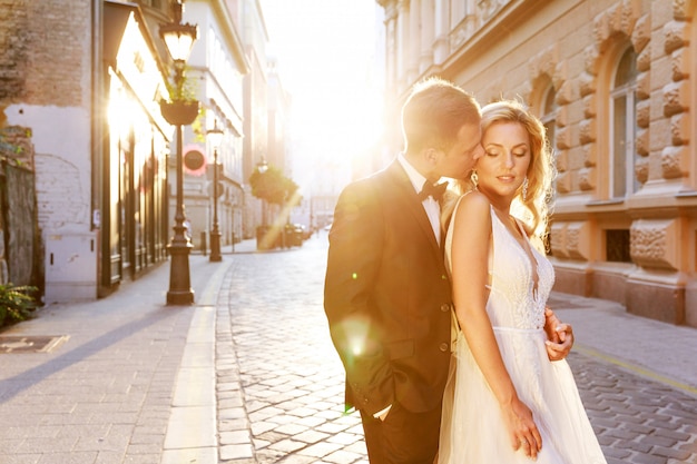 Bride and groom hugging in the old town street. Wedding couple in love. Luxury rhinestone dress.