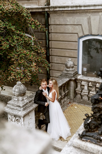 Foto abbracciare dello sposo e della sposa nella vecchia via della città. sposi innamorati. abito di strass di lusso.