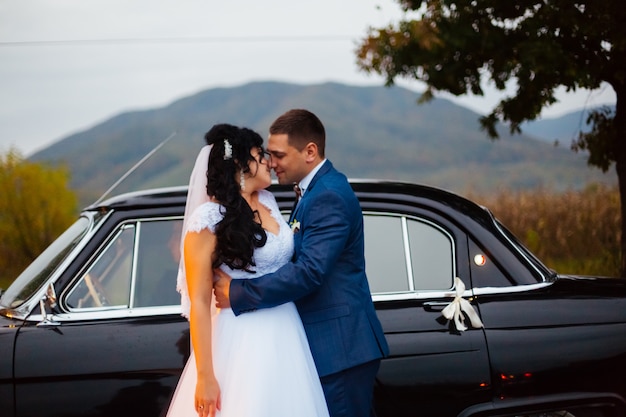 Foto abbracci dello sposo e della sposa nella parte anteriore della vecchia automobile