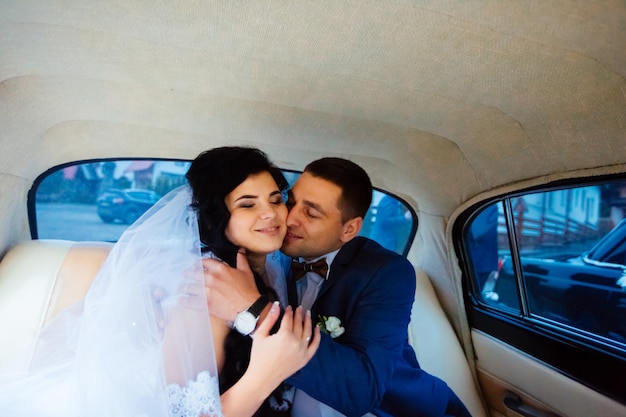 Bride and groom inside a classic car. They are happy.