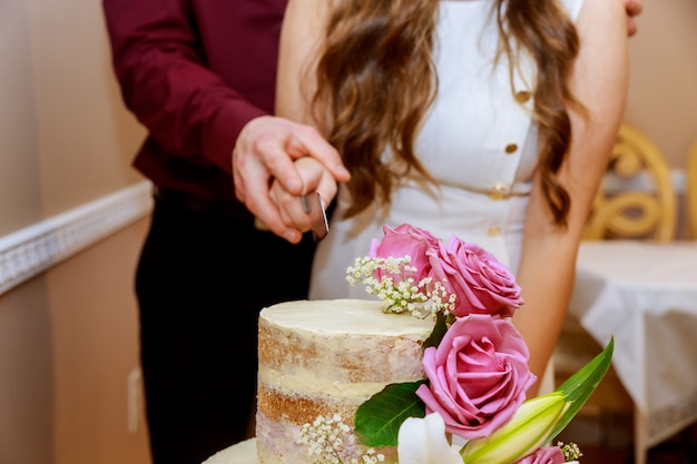 Bride and a groom is cutting wedding cake with pink roses