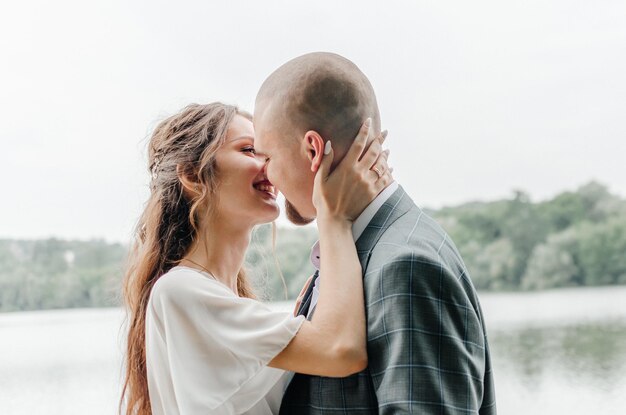 the bride and groom kiss on the shore of the lake