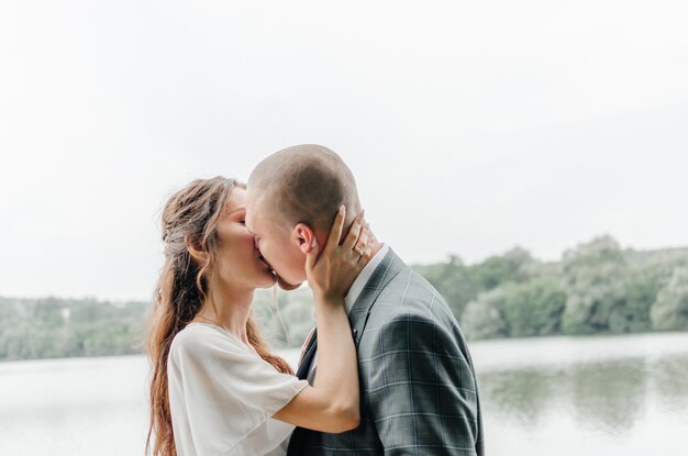 the bride and groom kiss on the shore of the lake