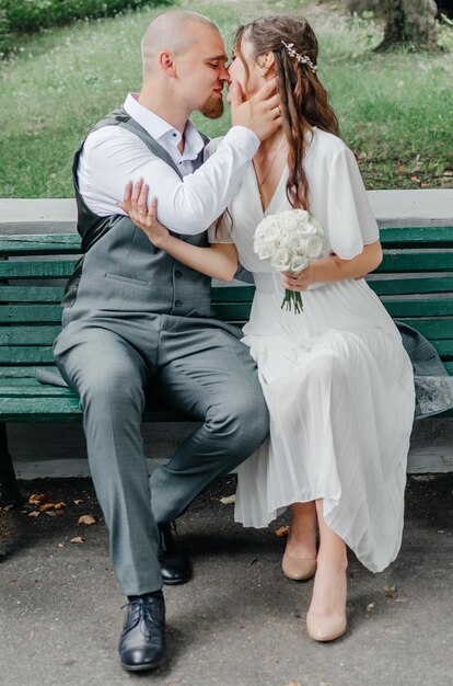 the bride and groom kiss while sitting on a bench