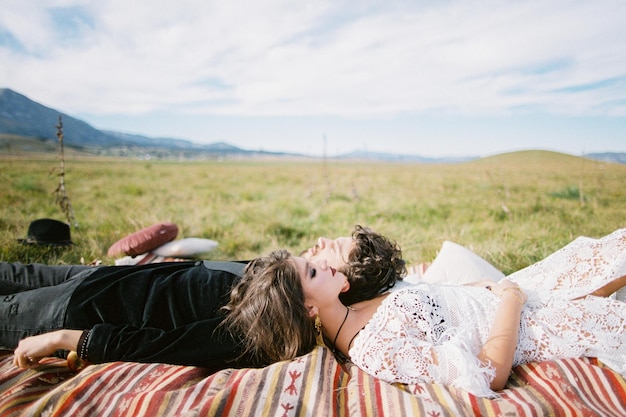 Photo bride and groom lie on a colorful bedspread on a green lawn