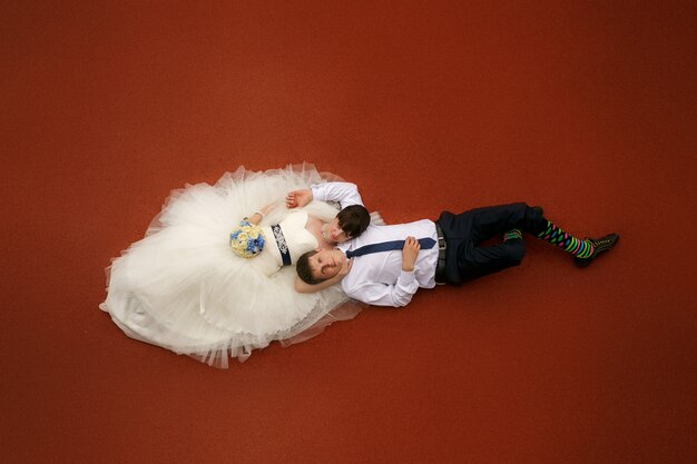 Bride and  groom lie on the red floor