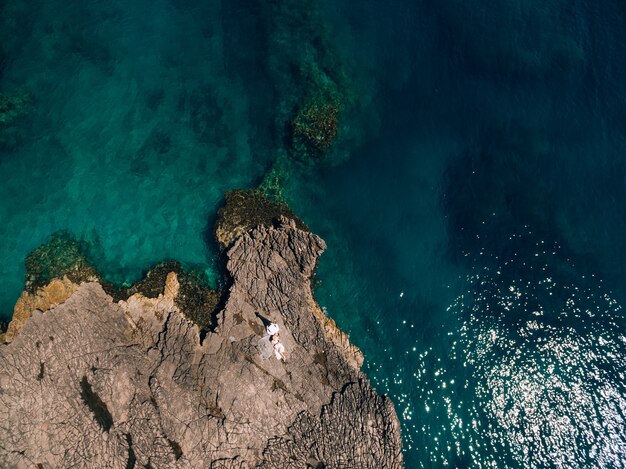 The bride and groom lie side by side on the rocky shore and look at each other top view