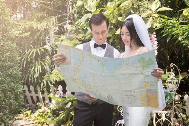 Foto la sposa e lo sposo guardano la mappa mentre stanno contro le piante