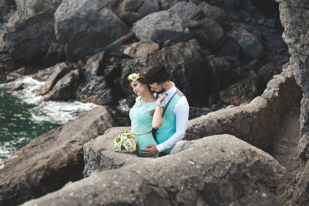 The bride and groom on nature in the mountains near the water. Suit and dress color Tiffany. Kiss and hug.