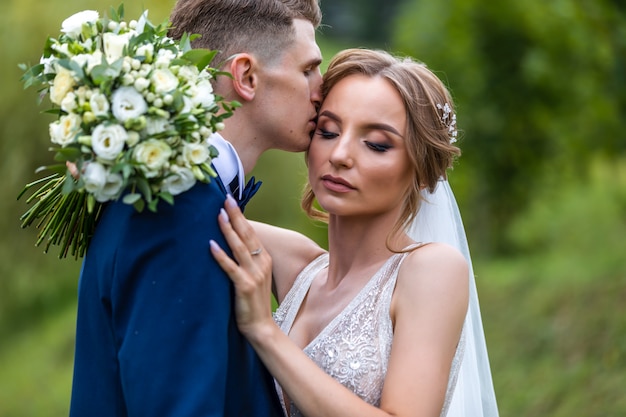 Bride and groom in a park kissing.couple newlyweds bride and groom at a wedding in nature green forest are kissing photo portrait. Wedding Couple