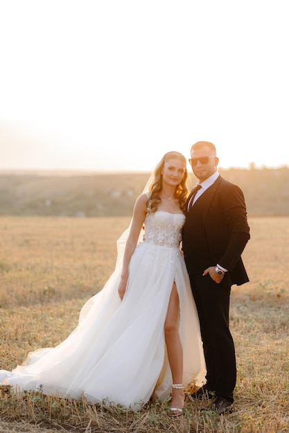 a bride and groom pose in a field with the sun behind them