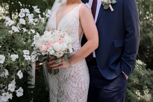 A bride and groom pose for a photo in front of a garden with white flowers.