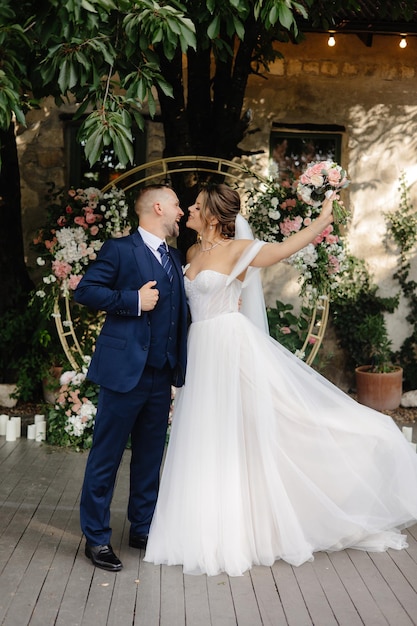 a bride and groom pose for a photo in front of a wall of flowers